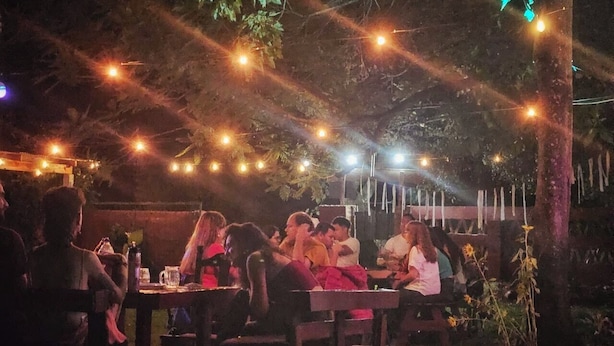 An outdoor dining area with tables and chairs, string lights overhead, and a wooden fence in the background. - Bungalow hostel Iguazù (Puerto Iguazú)