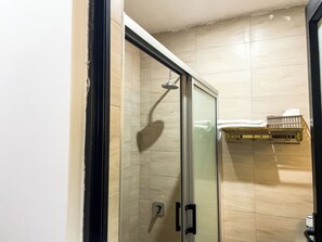 A glass-enclosed shower with a handheld showerhead, a towel rack with towels, and a small shelf with toiletries.