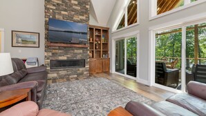 A spacious living room with a stone fireplace, comfortable seating, and large windows offering a view of the outdoors. - Lakefront: Hot tub, Dock, Firepit, Kayaks, Grill, Sleeps 13 (Henrico)