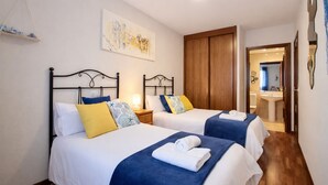 A hotel room with two beds, a wooden wardrobe, a bathroom visible through an open door, and a wall-mounted artwork. - Llanes Delux Apartment (Llanes)
