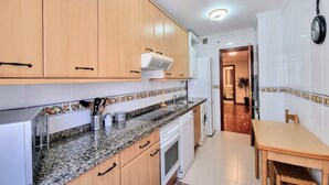 A kitchen with wooden cabinets, a granite countertop, a built-in oven, a dishwasher, and a dining area with a table and chairs. - Llanes Delux Apartment (Llanes)