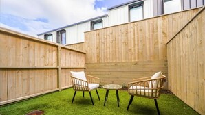 A fenced backyard with artificial grass, two wicker chairs, and a small round table. - Chic 2-Bedroom Retreat in Grey Lynn Minutes to CBD (Auckland)