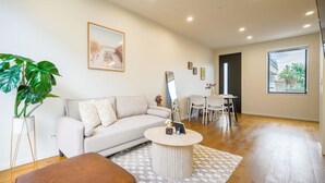 A modern living room with a sofa, a coffee table, a dining area with chairs, a large window, and a plant. - Chic 2-Bedroom Retreat in Grey Lynn Minutes to CBD (Auckland)