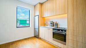 A modern kitchen with wooden cabinets, a built-in oven, and a window with a view of a green building. - Chic 2-Bedroom Retreat in Grey Lynn Minutes to CBD (Auckland)