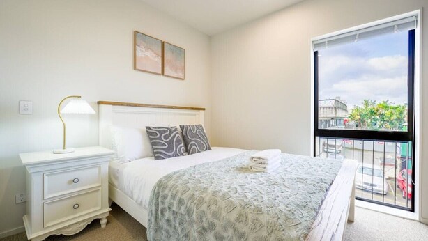 Un dormitorio con cama, mesita de noche, lámpara y vistas al exterior.