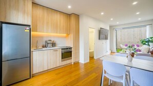 Una cocina moderna con armarios de madera, electrodomésticos de acero inoxidable y un comedor con mesa y sillas blancas.