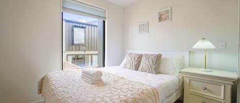Un dormitorio con una cama grande, una mesita de noche con lámpara y una ventana con persianas.