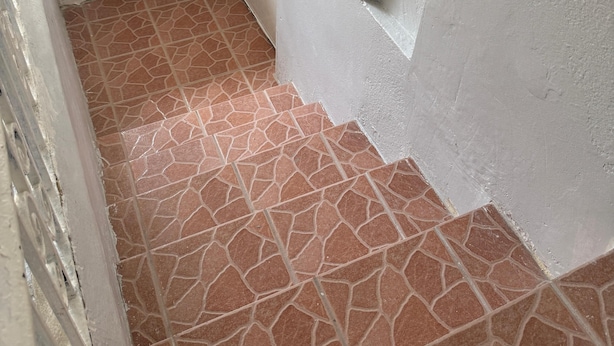 Un couloir étroit avec un sol carrelé, un mur blanc avec une fenêtre et une porte.