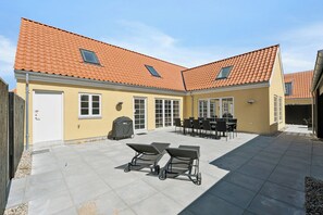 Un bâtiment à deux étages, doté d’un toit recouvert de tuiles, d’un patio couvert avec des meubles d’extérieur et d’une porte de garage.