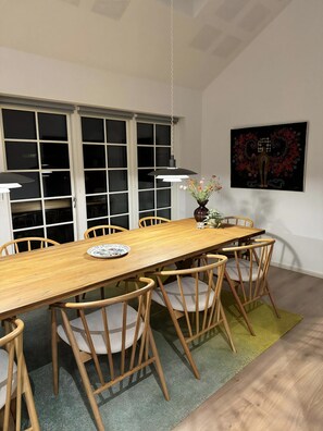Un coin repas avec une longue table en bois, six chaises, un vase de fleurs et un tableau accroché au mur.