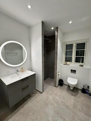 A modern bathroom with a white vanity, a round mirror, a shower, and a toilet.