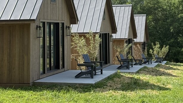Une rangée de chalets modernes dotés de toits en métal inclinés, de bardage en bois et de grandes fenêtres. Chaque chalet dispose d’un patio avec des meubles d’extérieur.