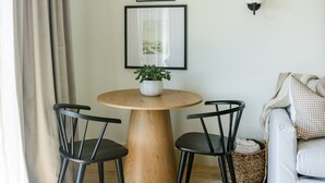Un coin repas avec une table ronde en bois, deux chaises noires et une plante en pot. Deux tableaux encadrés sont accrochés au mur, au-dessus de la table.