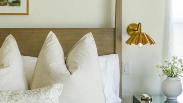Ein ordentlich bezogenes Bett mit drei Kissen, ein Nachttisch mit Lampe und eine Vase mit Blumen.