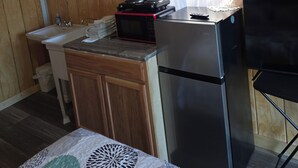 A compact kitchen with wooden walls, a sink, a microwave, a refrigerator, and a small table. - Cool cabin with AC in Kelso (Kelso)