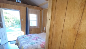 A wooden room with a bed, a window, and a door leading outside. - Cool cabin with AC in Kelso (Kelso)