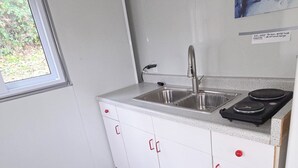 Uma cozinha compacta com janela, pia, fogão e armários brancos.