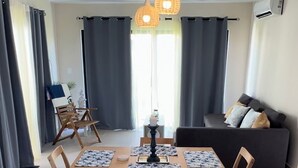 A modern dining area with a wooden table and chairs, a black rug, and pendant lighting.