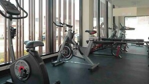 A gym with stationary bikes and cardio equipment, large windows, and a mirrored wall.