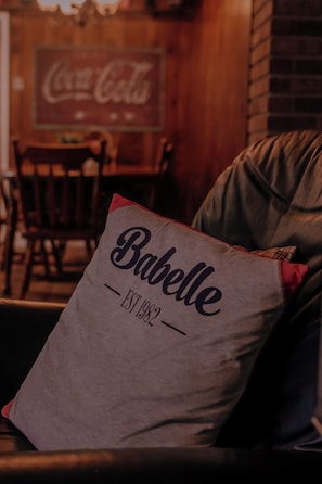 A pillow with the text 'Babelle EST 1982' on a couch in a room with a brick wall and a Coca-Cola sign in the background. - Delightful 4-bedroom house in Blairsville (Blairsville)
