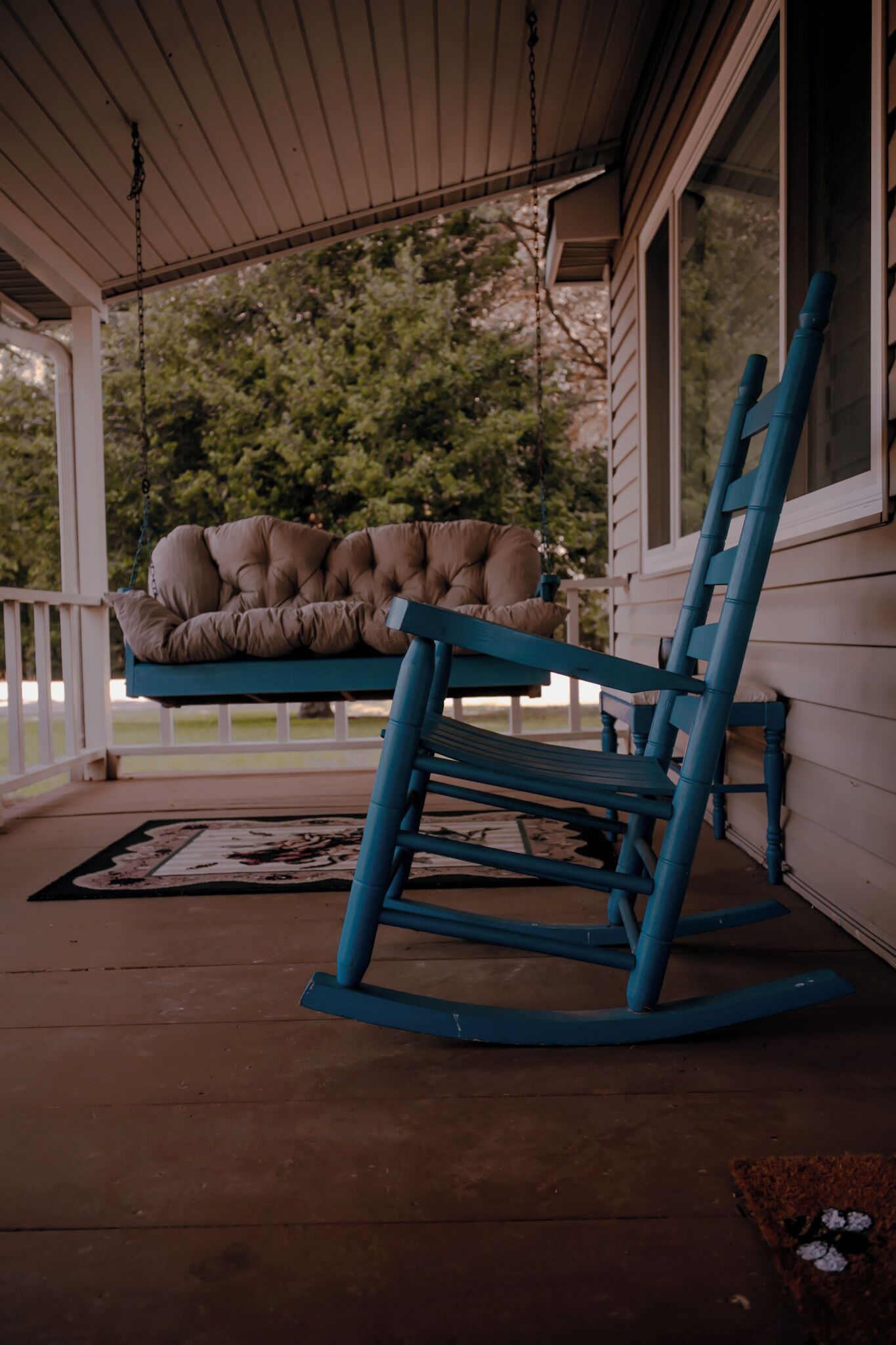 Eine Veranda mit Schaukelstuhl und gepolstertem Sitzplatz.