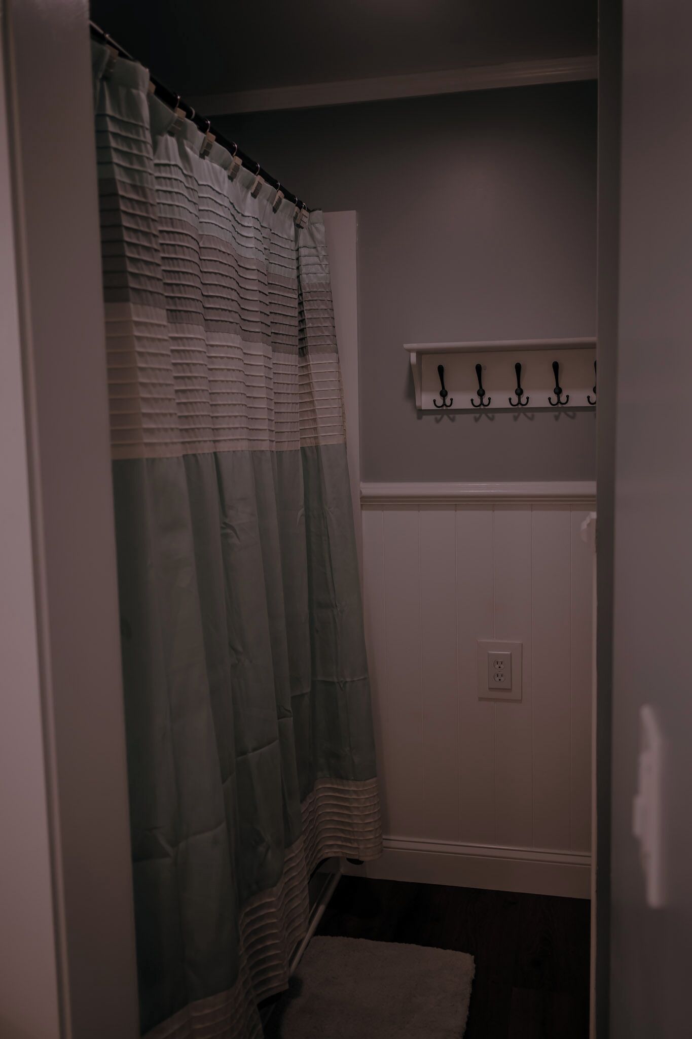A bathroom with a shower curtain, a towel rack, and a wall-mounted light switch.