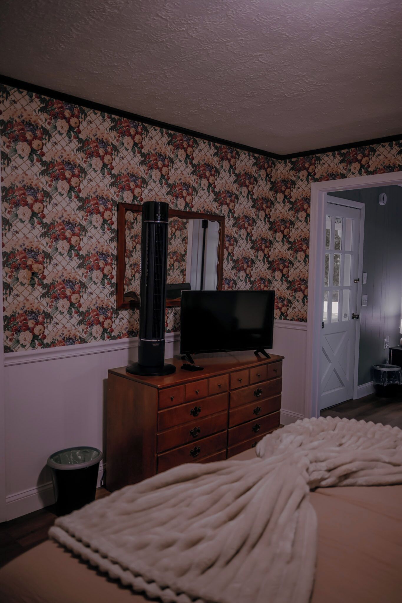 Ein Schlafzimmer mit Fernseher auf einer Kommode, einer Tür und blumigem Wandpapier.
