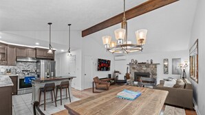 A modern kitchen with a central island, wooden dining table, and a cozy living area with a fireplace. - Near pool & beach. Private Hot Tub. AC, Firepit (Pocono Lake)