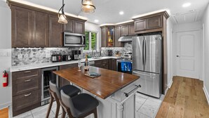 A modern kitchen with dark wood cabinets, stainless steel appliances, a marble countertop, and pendant lighting. - Near pool & beach. Private Hot Tub. AC, Firepit (Pocono Lake)