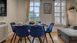 Un coin repas avec une table dressée pour quatre personnes, des chaises bleues et un panier de fruits posé sur la table.