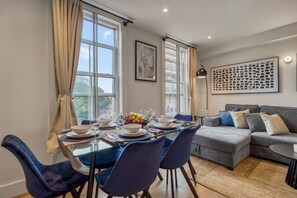 Een eetgedeelte met een glazen tafel voor zes personen, blauwe stoelen en een grijze bank op de achtergrond.