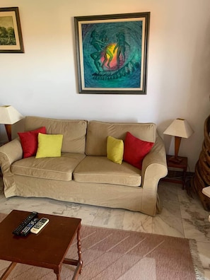 Un canapé beige agrémenté de coussins rouges et jaunes, une table basse en bois et deux lampes placées de part et d’autre.