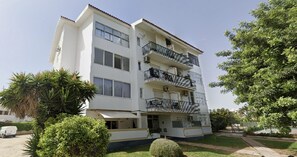 Un immeuble résidentiel à plusieurs étages, doté de balcons, d’un espace de stationnement et entouré de verdure.