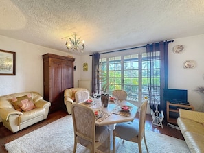 A living room with a dining area, a sofa, a television, and a window with curtains.