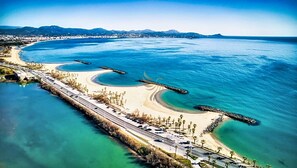 An aerial view of a coastal area with a long road, a beach, and a clear blue sea.