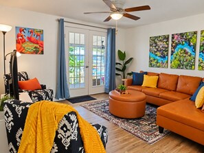 A living room with a sofa, armchair, ottoman, and a ceiling fan.