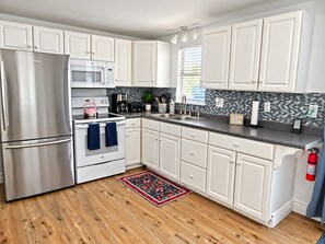 A kitchen with white cabinets, stainless steel appliances, a tiled backsplash, and a wooden floor.