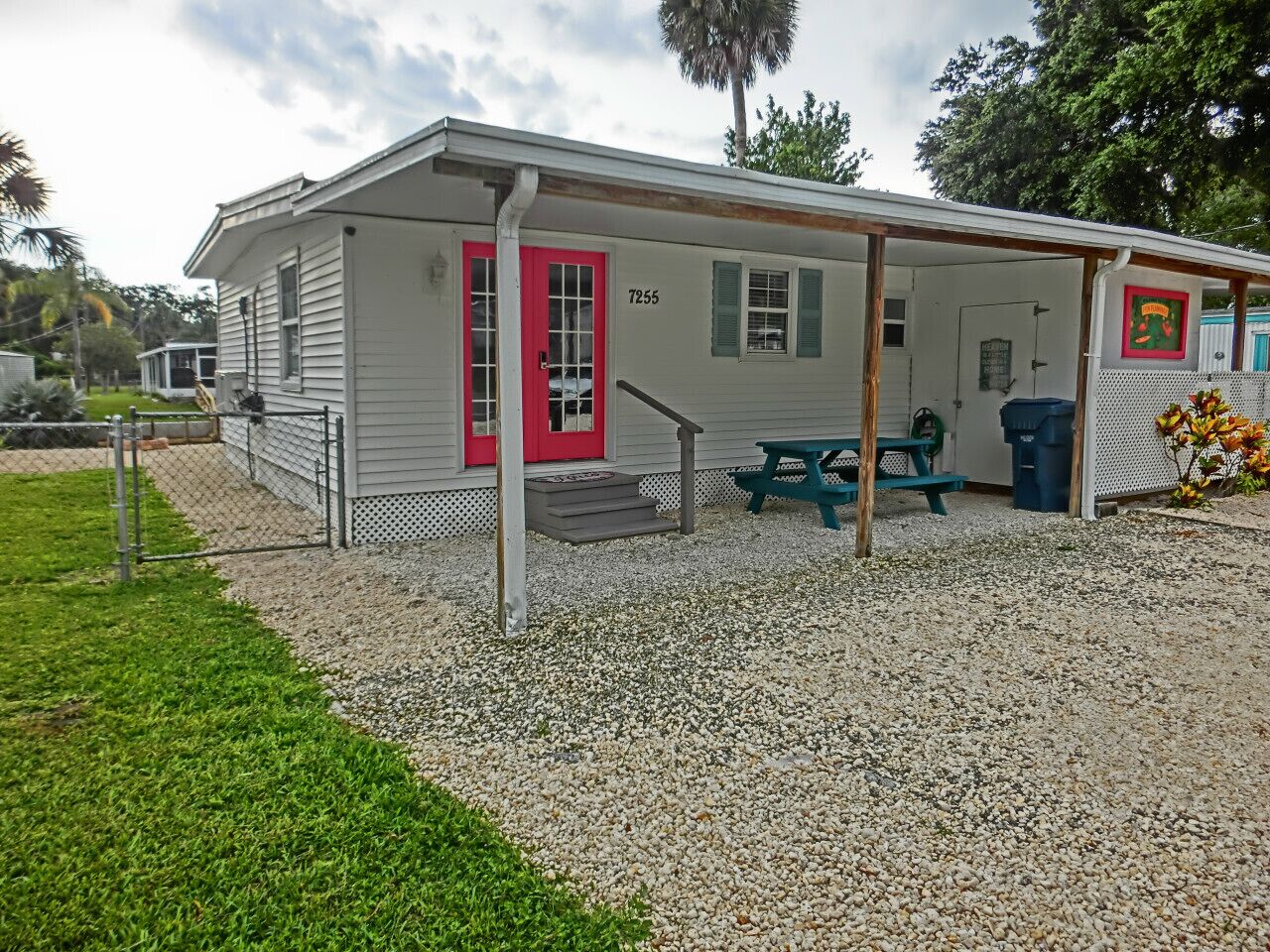 A single-story building with a red door, numbered 7255, featuring a covered outdoor seating area with a picnic table and a trash bin.