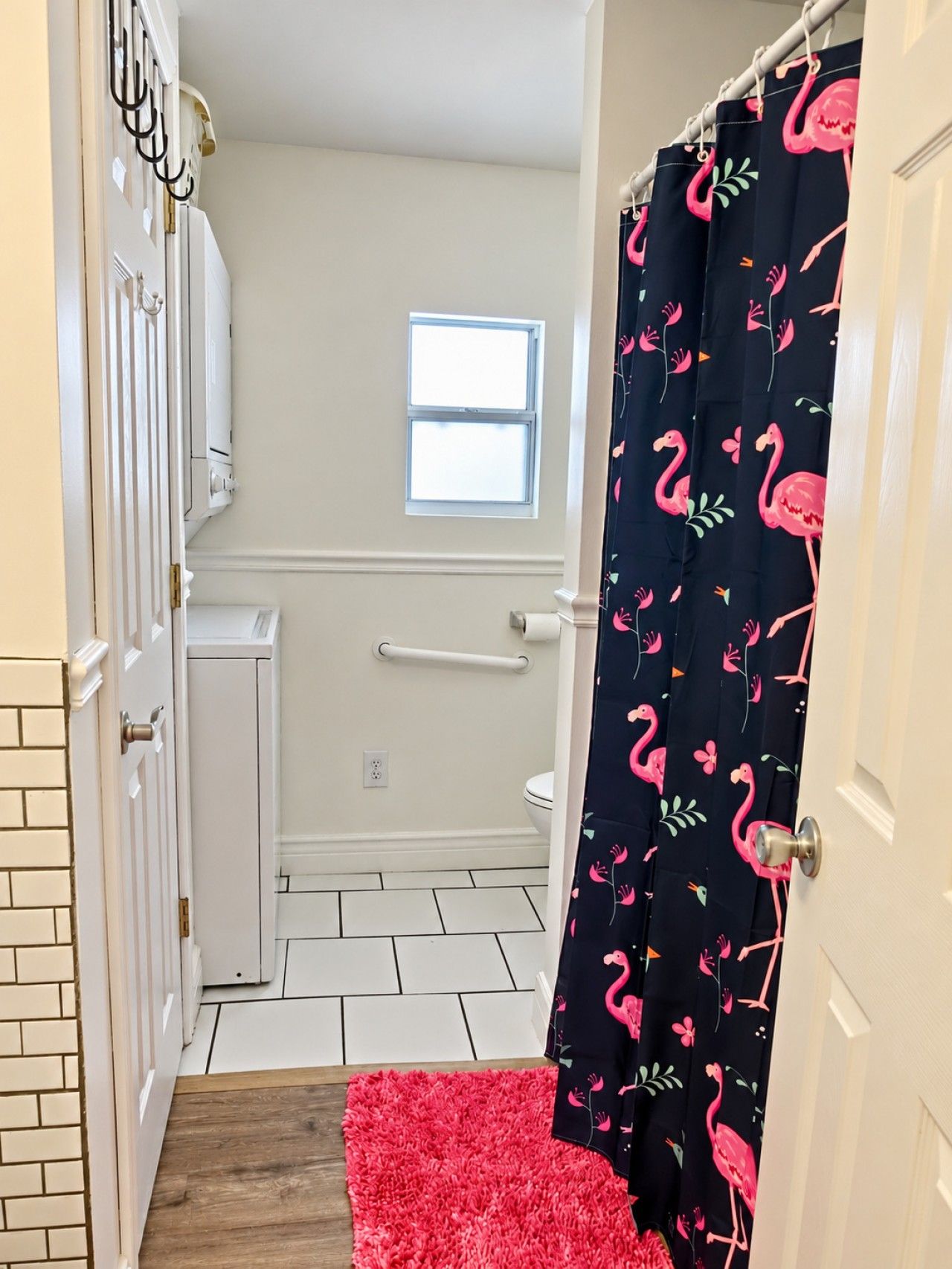 Une salle de bain avec une porte blanche, une fenêtre, un radiateur blanc, des toilettes blanches et un tapis rouge.