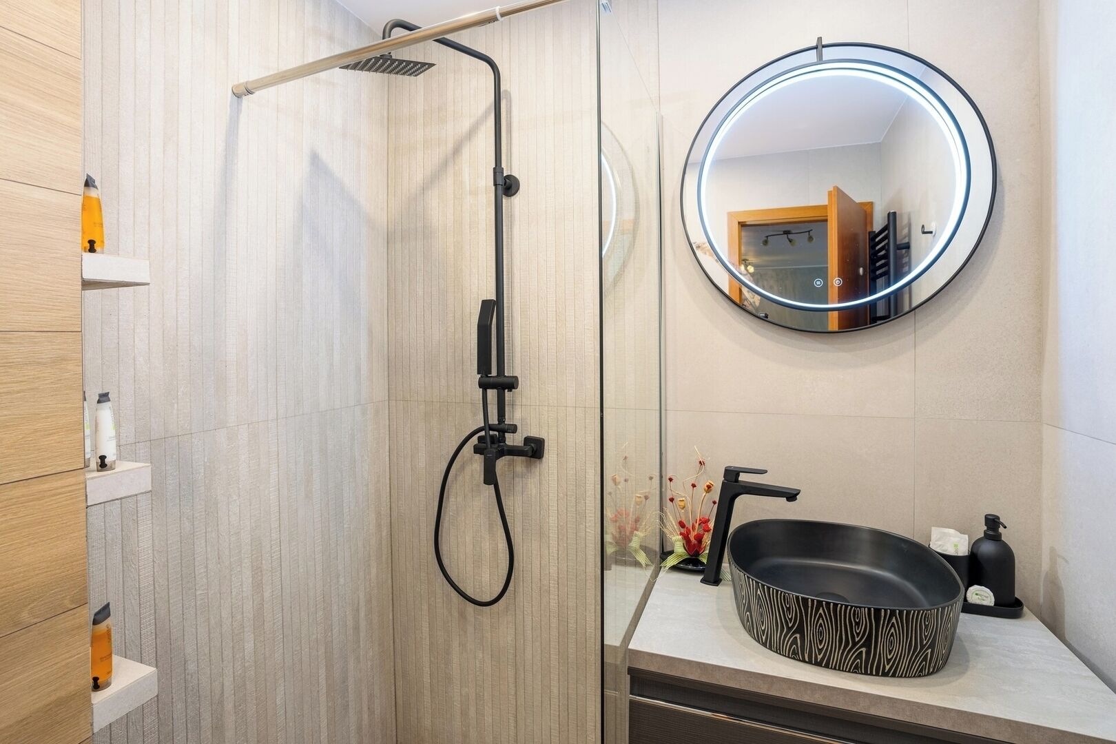 Stylish bathroom equipped with walk-in shower, black sink, round led mirror, toilet, free toiletries to enjoy a spa-like experience 