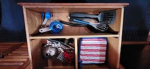 A wooden storage unit with kitchen utensils, a whisk, scissors, and a striped cloth.