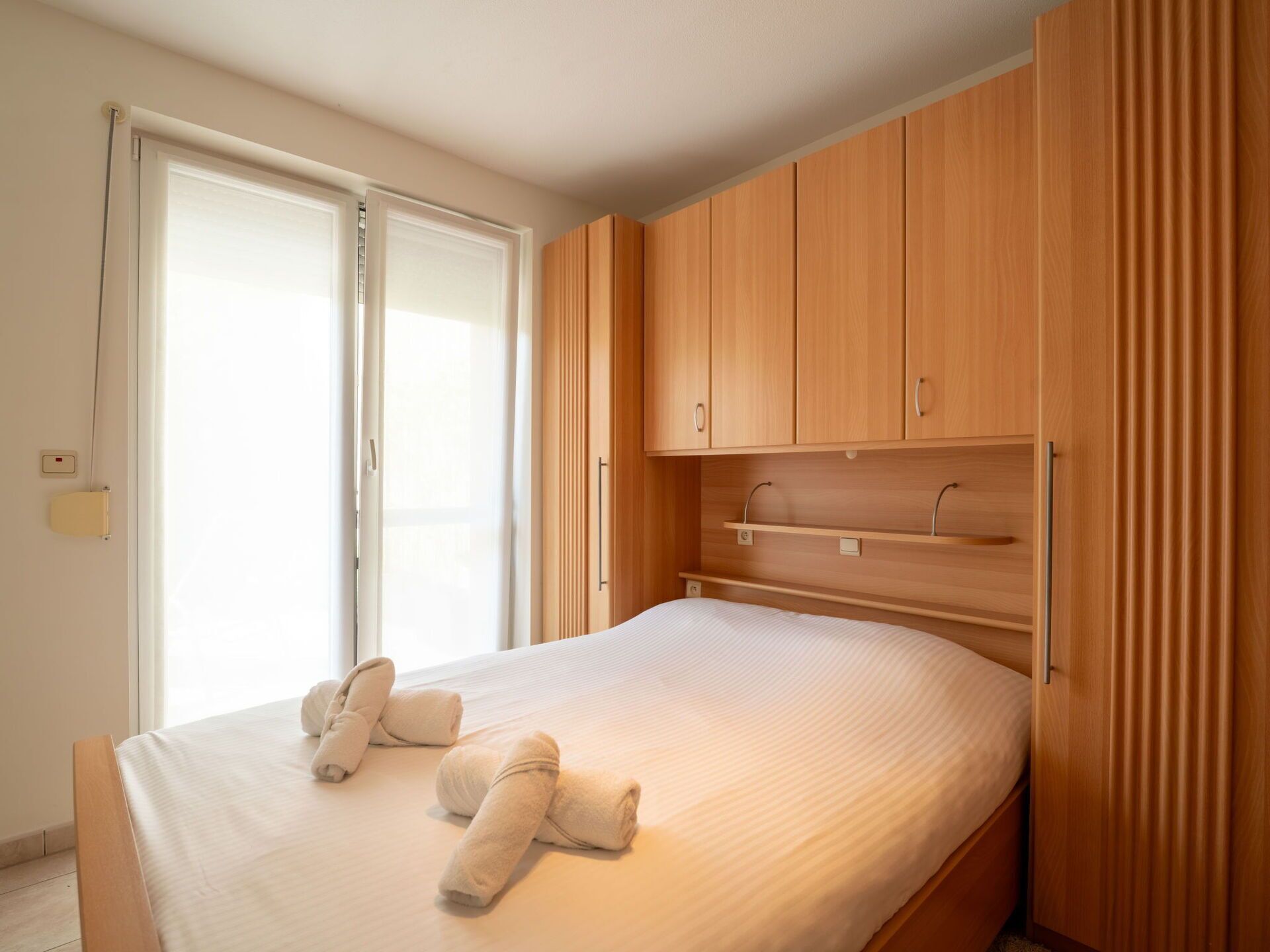 A bedroom with a bed, wooden wardrobe, and a sliding door.