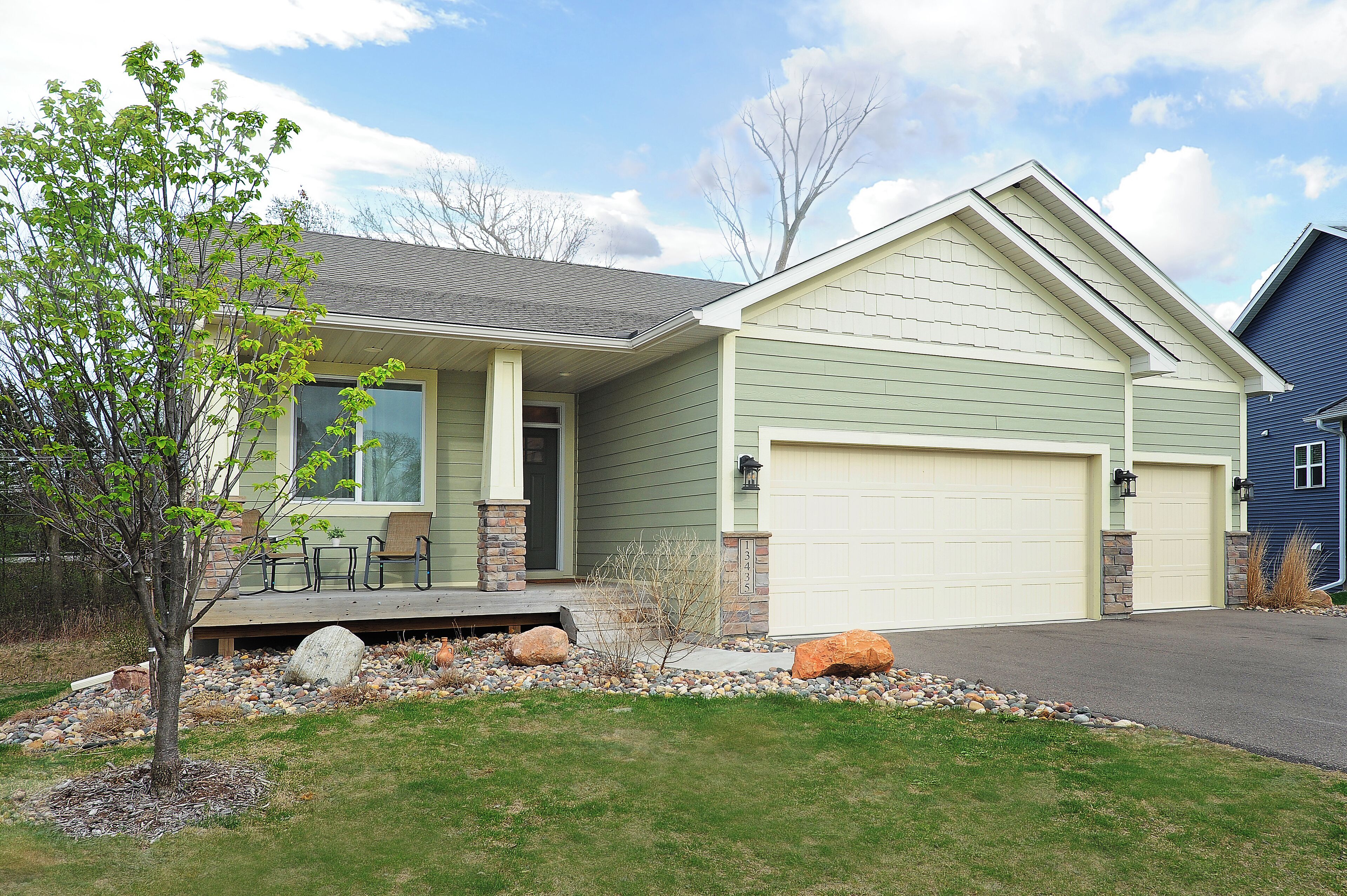 A two-story house with a front porch, a garage, and a small garden area with rocks and a tree.