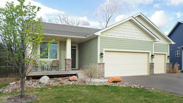 A two-story house with a front porch, a garage, and a small garden area with rocks and a tree.