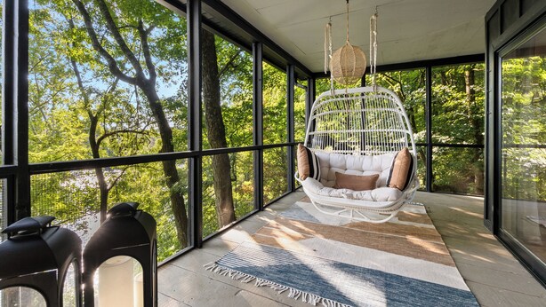 A spacious balcony with large windows, a hanging chair, and a striped rug. - *NEW* Waterfront Treehouse - Sweeping Views on 2.5 Acres (Knoxville)