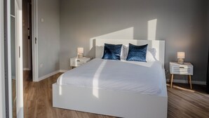 A modern bedroom with a large bed, two bedside tables with lamps, and a wooden floor. - 3BR Flat by Casa da Música | Central, Sleeps 6 | D (Porto)