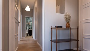 A hallway with a wooden floor, a metal shelf with a vase, and a mirror on the wall. - 3BR Flat by Casa da Música | Central, Sleeps 6 | D (Porto)