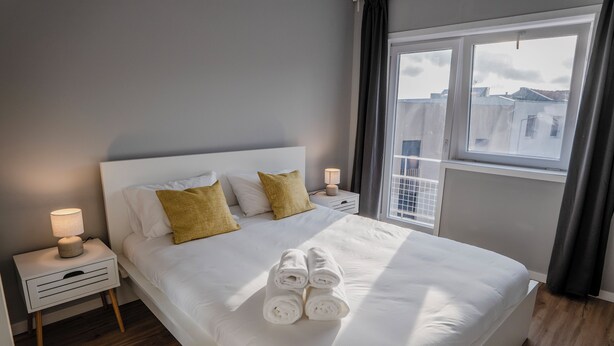A neatly made bed with rolled towels, a bedside lamp, and a window with curtains. - 3BR Flat by Casa da Música | Central, Sleeps 6 | D (Porto)