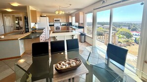A modern kitchen with a central island, a dining area with a glass table, and a large sliding glass door to a balcony with a scenic view.