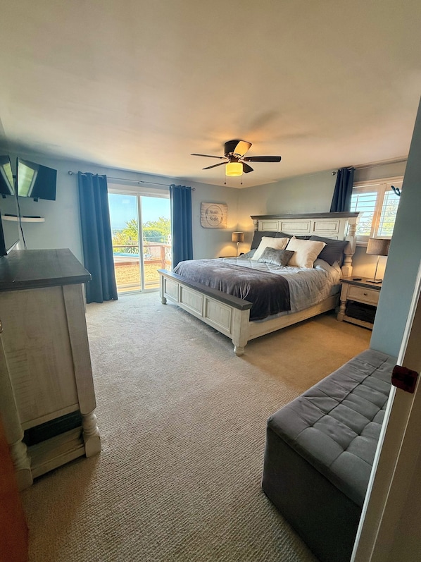 A bedroom with a bed, a desk, a chair, a ceiling fan, and a view of the outdoors. - Luxurious Hilltop Home w/ Private Hot Tub and Direct Dune Access (Winchester Bay)